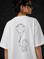 A woman wearing an oversized white t-shirt, viewed from the back. The shirt features a minimalist black line art graphic of a person holding a balloon globe.